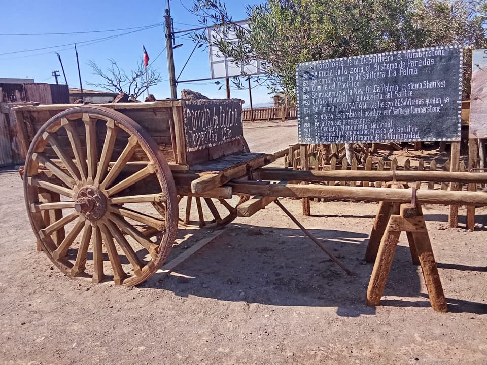 Carreta de caliche con ruedas de madera junto al panel con la cronología de la oficina salitrera