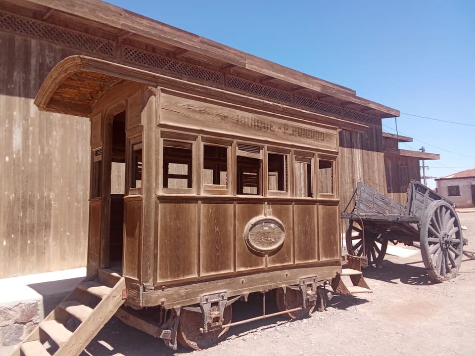 Coche de pasajeros de madera con el letrero Iquique - P. Hundido y una carreta al costado