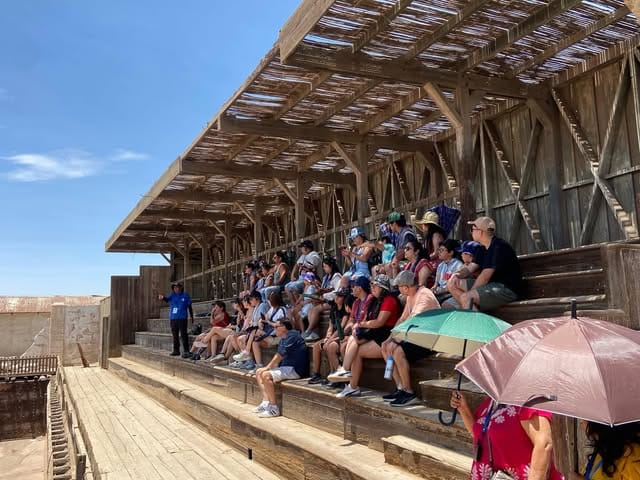 Grupo sentado en las gradas de madera de Humberstone escuchando al guía, de polera azul, a la izquierda